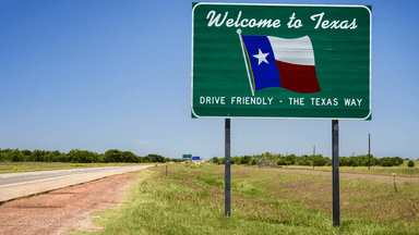 Welcome to Texas sign alongside a highway with green fields in the background